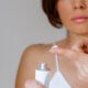 A woman presses the ointment onto her finger and applies it to the bite site by a bedbug on her shoulder on a white background, close-up. Skin health problem. Red pimples.