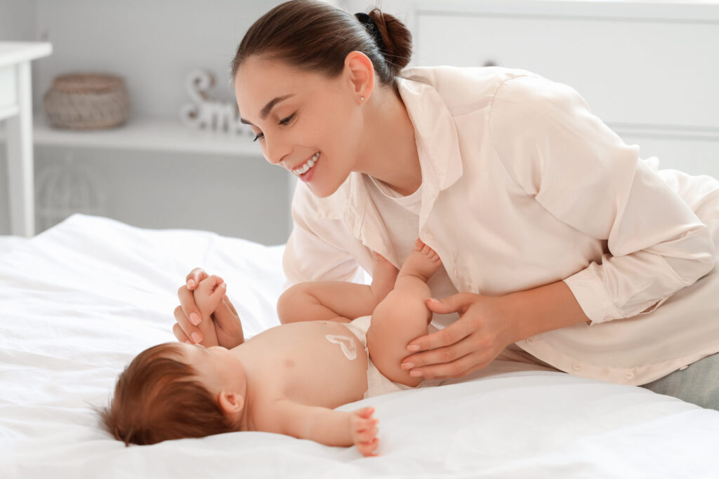 Cute little baby with heart made of cream and mother lying on bed