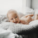 Naked newborn boy lies on the soft blanket before a bright windo