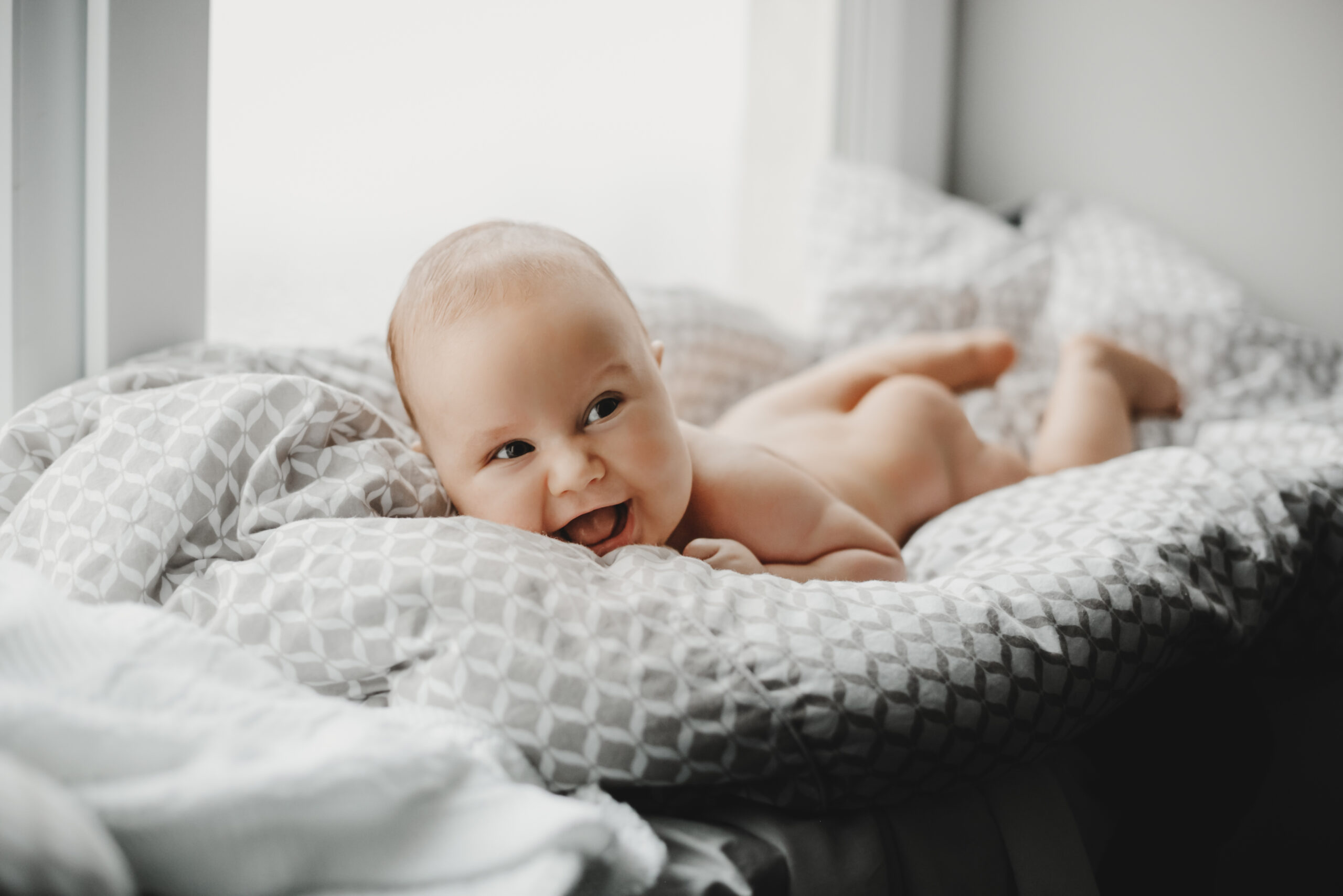 Naked newborn boy lies on the soft blanket before a bright windo
