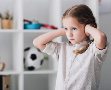 close-up portrait-of-sad little-child-covering-ears-with-hands-and-looking-away