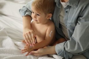 Mother_applying cream_onto_her_baby's_body_on_bed_at_home,_closeup