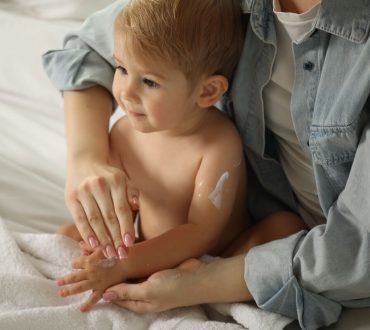 Mother_applying cream_onto_her_baby's_body_on_bed_at_home,_closeup